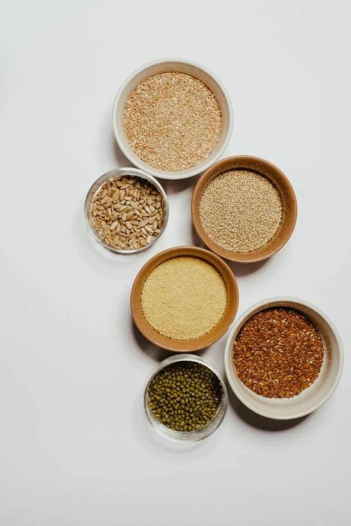 Top view of various seeds and grains displayed in ceramic bowls on a white background.